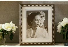 two vases with white flowers in front of a black and white photo on a shelf