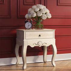 a white table with a clock and flowers on it in front of a red wall