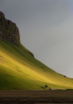 two sheep are grazing on the grass in front of a large rock formation and green hills