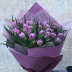 a bouquet of pink tulips wrapped in purple paper with greenery on top