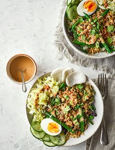 two bowls filled with rice, cucumbers and eggs on top of a table