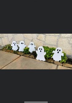 three white ghost decorations in front of a stone wall with green plants and grass on the ground