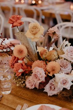 an arrangement of flowers on a table in front of chairs and tables with place settings