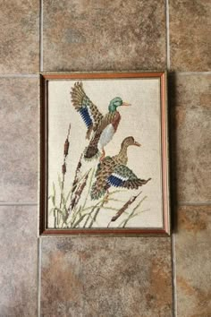 two ducks sitting on top of a tile floor next to tall grass and reeds