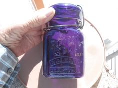 a person holding a purple mason jar on top of a table