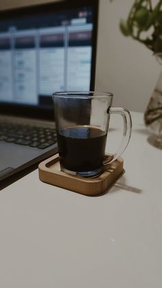 a cup of coffee sitting on top of a wooden coaster next to a laptop computer