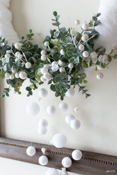 some white balls and greenery are hanging on the wall