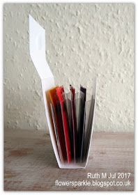 a stack of different colored papers sitting in a glass vase on a table next to a white wall