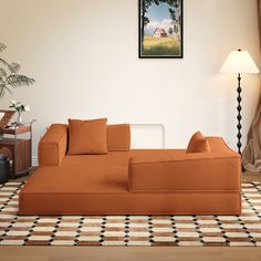 an orange couch sitting on top of a wooden floor next to a lamp and window