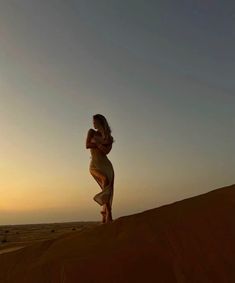 a woman standing on top of a sand dune in the middle of the desert at sunset