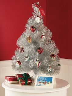 a white christmas tree with red and green ornaments on it's top, next to presents