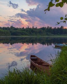 two canoes sitting on the shore of a lake at sunset with clouds in the sky