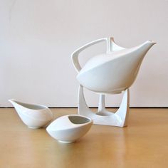 three white bowls sitting on top of a wooden table next to a vase and bowl