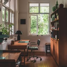 a room with a desk, chair and bookshelf next to a large window