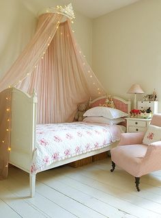 a pink canopy bed in a girls'bedroom with white furniture and lights on the ceiling