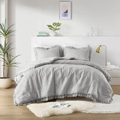 a bedroom with white walls and wooden flooring has a gray comforter on the bed