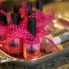 three nail polish bottles in a tray with pink bows on it and two pens next to them