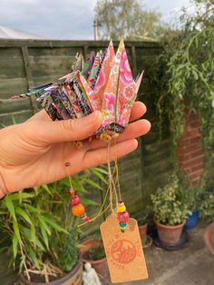 a person holding up a small origami crane in their left hand with tags attached to it