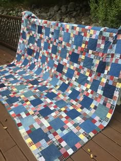 a blue and red patchwork quilt sitting on top of a wooden deck next to trees