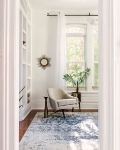 a living room with white walls and a large rug on the floor in front of a window