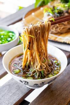 chopsticks sticking out of a bowl of noodles on a table with bowls of vegetables