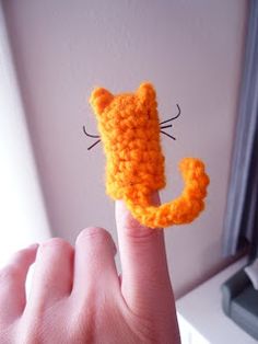 a hand is holding up a tiny crocheted cat