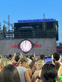 a crowd of people standing in front of a stage with a large clock on it