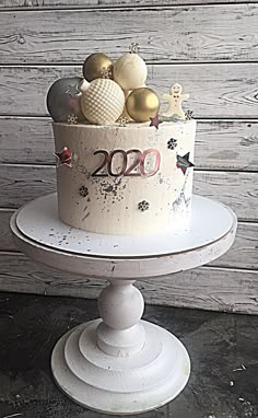 a white cake with gold and silver decorations on it sitting on a pedestal in front of a wooden wall