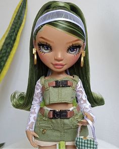 a doll with green hair and blue eyes wearing overalls, holding a handbag