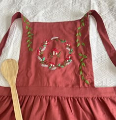 a red apron with green leaves on it and a wooden spoon