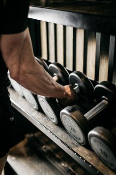 a man is lifting dumbs on a rack with other dumbs in the background