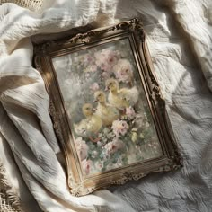 an old framed painting with ducklings and flowers on a white bed linens background