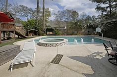 an empty swimming pool with lounge chairs and umbrellas around it, surrounded by trees