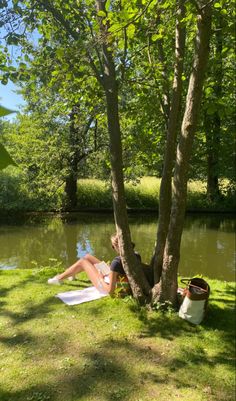 a woman laying on top of a white towel under a tree next to a river