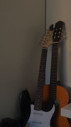 an electric guitar sitting on top of a wooden floor next to a black and orange guitar