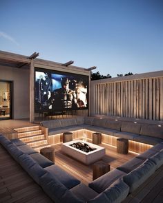 a large couch sitting on top of a wooden floor next to a fire pit in front of a movie screen