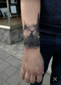 a man's arm with a deer and forest scene tattoo on the left wrist