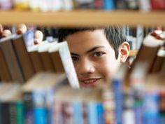 a young man is smiling while looking through the bookshelves in a library,