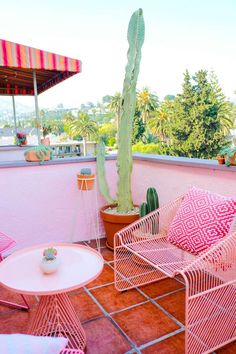 two chairs and a table on a balcony with a cactus in the corner next to them