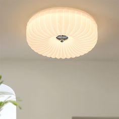 a white ceiling light hanging from the ceiling above a table with a vase on it