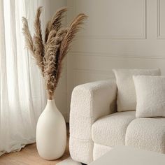 a white vase with some dry grass in it sitting on a table next to a couch