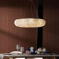 a chandelier hanging over a dining room table with flowers on the sideboard