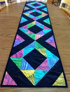 a long table runner with colorful quilts on the top and bottom, along with chairs