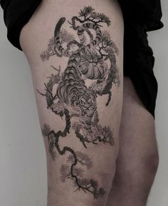 a woman's thigh with a tiger tattoo on her leg and tree branches in the background