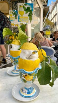 three lemons are sitting in glass vases on a table with people seated around