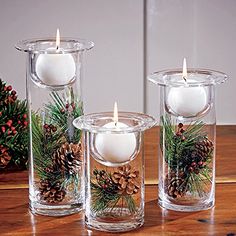 three clear glass vases filled with candles and pine cones