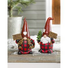 two christmas gnomes with signs on their heads sitting in the snow next to a potted plant