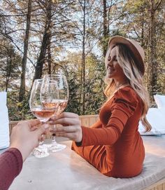 two women toasting with wine glasses in front of them on a table surrounded by trees