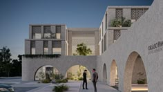 two men are standing in front of a building with arches and plants on the side