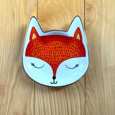 a bowl with a red and white fox design on it's face sitting on a wooden surface